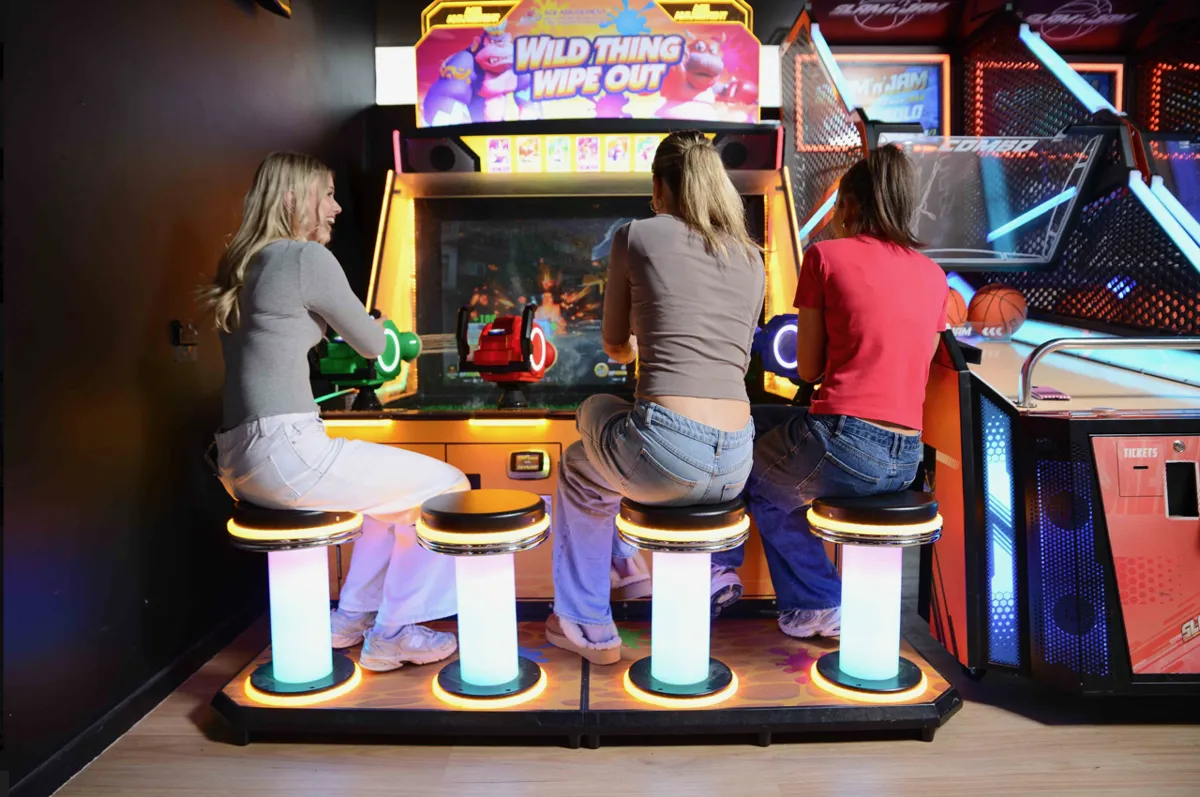 Three friends playing a water-gun arcade game on glowing stools at Bendigo Bowl